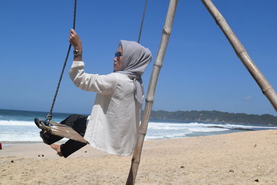 Woman on swing at beach against blue sky