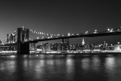 Illuminated brooklyn bridge over east river against sky