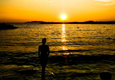 Silhouette of man standing in sea during sunset