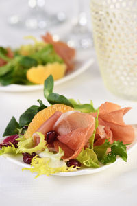 Portioned appetizer of prosciutto ham served on a of mixed with orange and pomegranate.