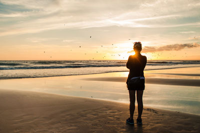 Silhouette woman standing on beach against sky during sunset