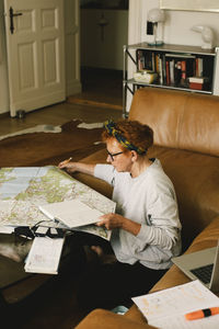 Side view of elderly woman planning trip on map while sitting in living room at home