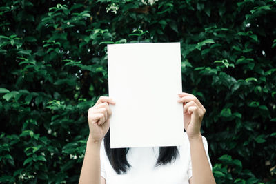 Midsection of person holding paper against white wall