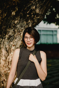 Portrait of a smiling young woman standing on tree trunk