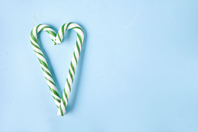 Green and white candy cane in the shape of heart on the blue background.