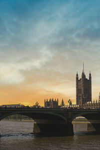 Bridge over river in city against sky during sunset