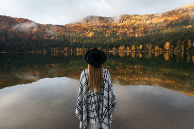 Caucasian woman standing in a poncho and hat. autumn in colorful forest near the lake.travel concept