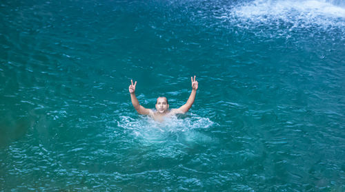 Young man swimming at natural waterfall blue water at morning from top angle