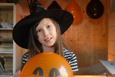 Portrait of adorable teen girl wearing halloween hat holding ballon and smiling. halloween home