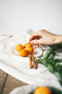 Hand reaches out to take a tangerine, christmas fruit lies on the table with cinnamon and spruce