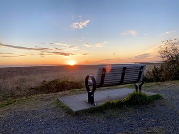 Bench on field against sky during sunset