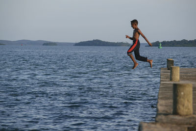 Side view of shirtless boy jumping in sea from pier