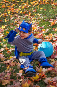 Smiling boy in a halloween costume, sitting in the fall leaves with his candy bucket