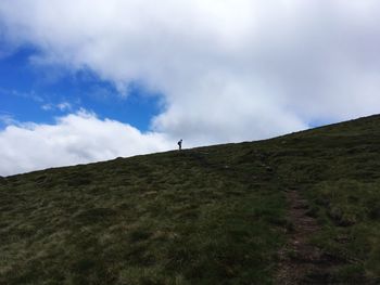 Low angle view of hiker walking on mountain against cloudy sky