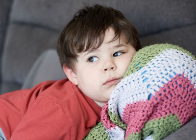 Portrait of a young boy resting on the couch with his head on a ball inside his blanket