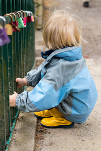 Rear view of boy holding umbrella against fence