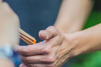 Cropped hands of people burning incense sticks outdoors