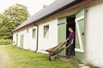 Man pushing wheelbarrow while coming out of barn at farm