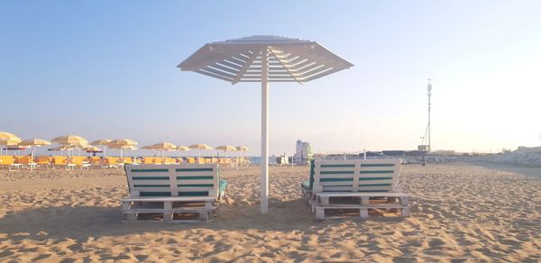 Empty lounge chairs by parasol at beach against sky