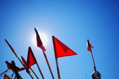 Low angle view of red flags against clear blue sky on sunny day