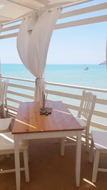 Empty chairs and tables at beach against sky