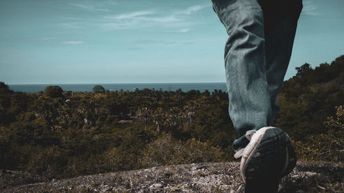 Low section of man walking on rock against sky