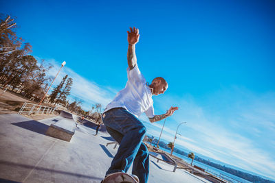Man skateboarding against blue sky during sunny day