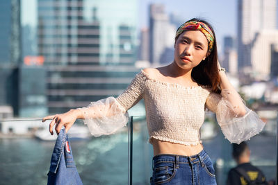 Young woman looking away while standing against city in background