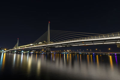 Illuminated bridge over river against sky at night