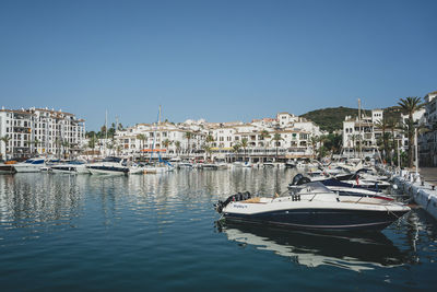 Sailboats moored in harbor by buildings against clear sky
