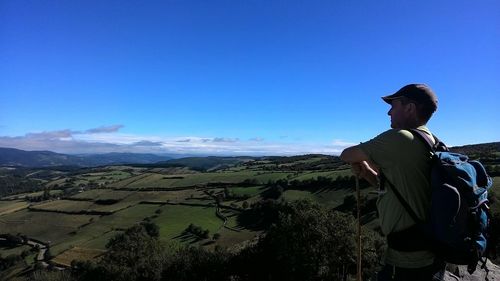 Rear view of man standing on landscape against clear blue sky