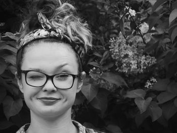 Close-up portrait of smiling young woman winking against plants at park