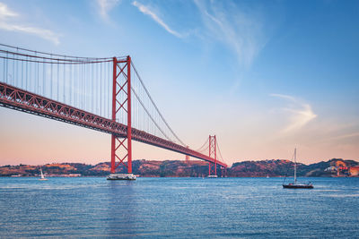 View of 25 de abril bridge over tagus river, christ the king and boat at sunset. lisbon, portugal