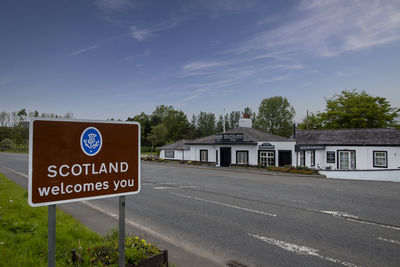 Road sign by building against sky