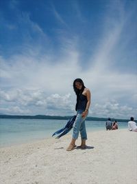 Portrait of young woman standing on beach against sky