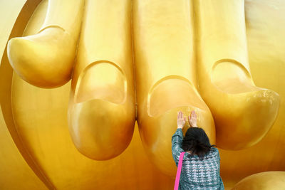 Reaar view of woman praying while standing by statue in temple