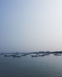 Boats in calm sea against clear sky