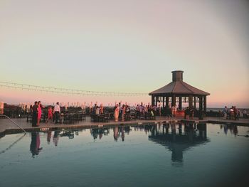 People by swimming pool against clear sky during sunset