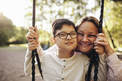 Portrait of smiling mother with son playing on swing at playground