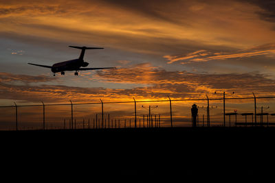 Silhouette airplane flying over runway against sky during sunset