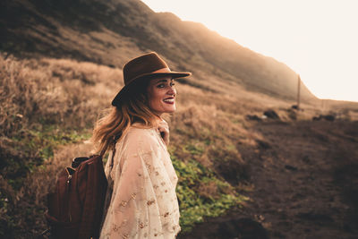 Side view portrait of woman wearing hat while standing on land during sunset