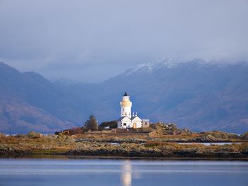 Lighthouse amidst buildings and mountains against sky