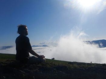 Man sitting on rock against sky