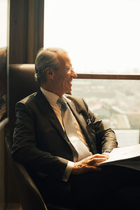 Smiling mature lawyer with documents looking through window at office