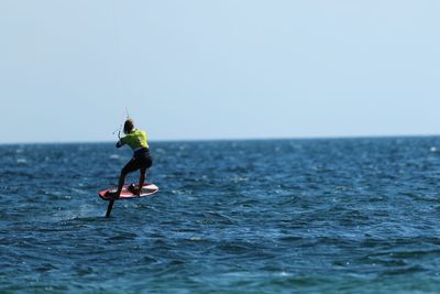 Woman kiteboarding in sea against clear sky