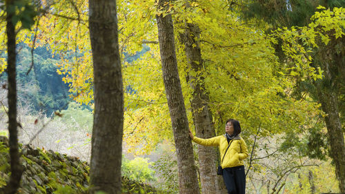 Rear view of woman standing by trees in forest during autumn
