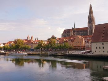 View of buildings by river against sky in city