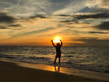 Silhouette woman standing on beach against sky during sunset