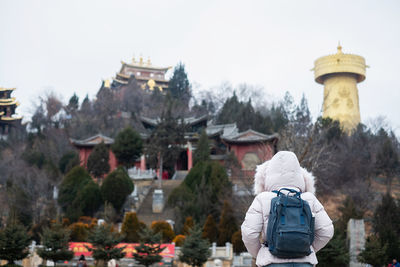 Rear view of man by building against sky during winter