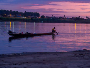 Silhouette man on boat in lake against sky during sunset